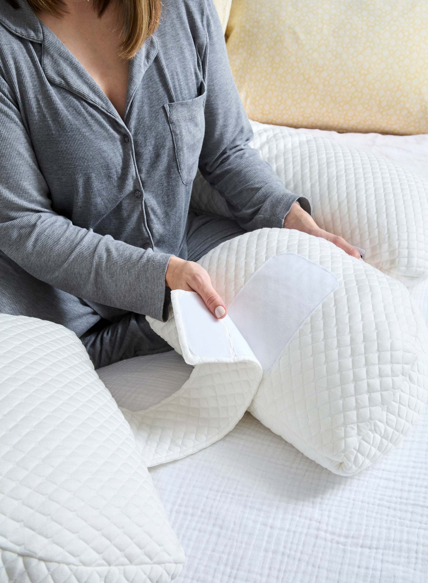 Person holding a white pregnancy pillow on a bed