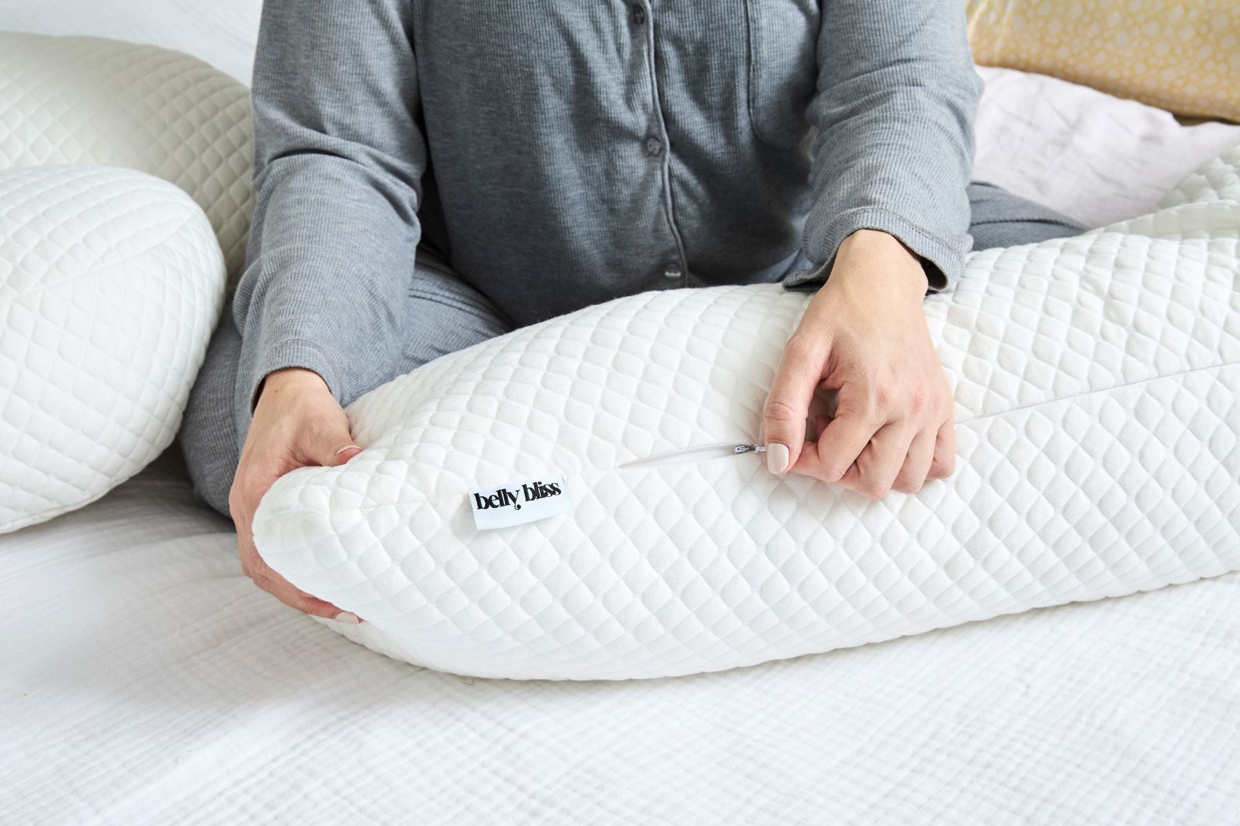 Person holding a white pregnancy pillow with 'belly bliss' branding on a bed.