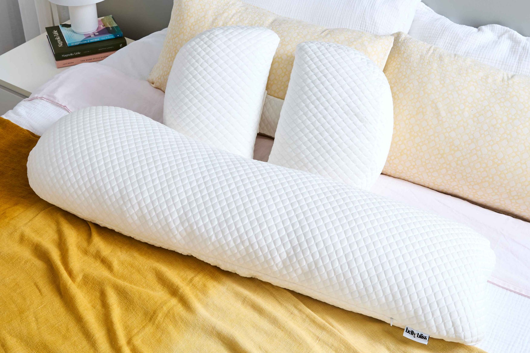 White pregnancy pillow on bed with yellow blanket