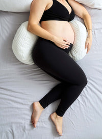Pregnant person using a wedge-shaped pillow on a bed