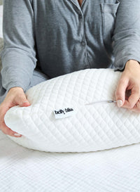 Person holding a white belly pillow with 'belly bliss' label on a bed.