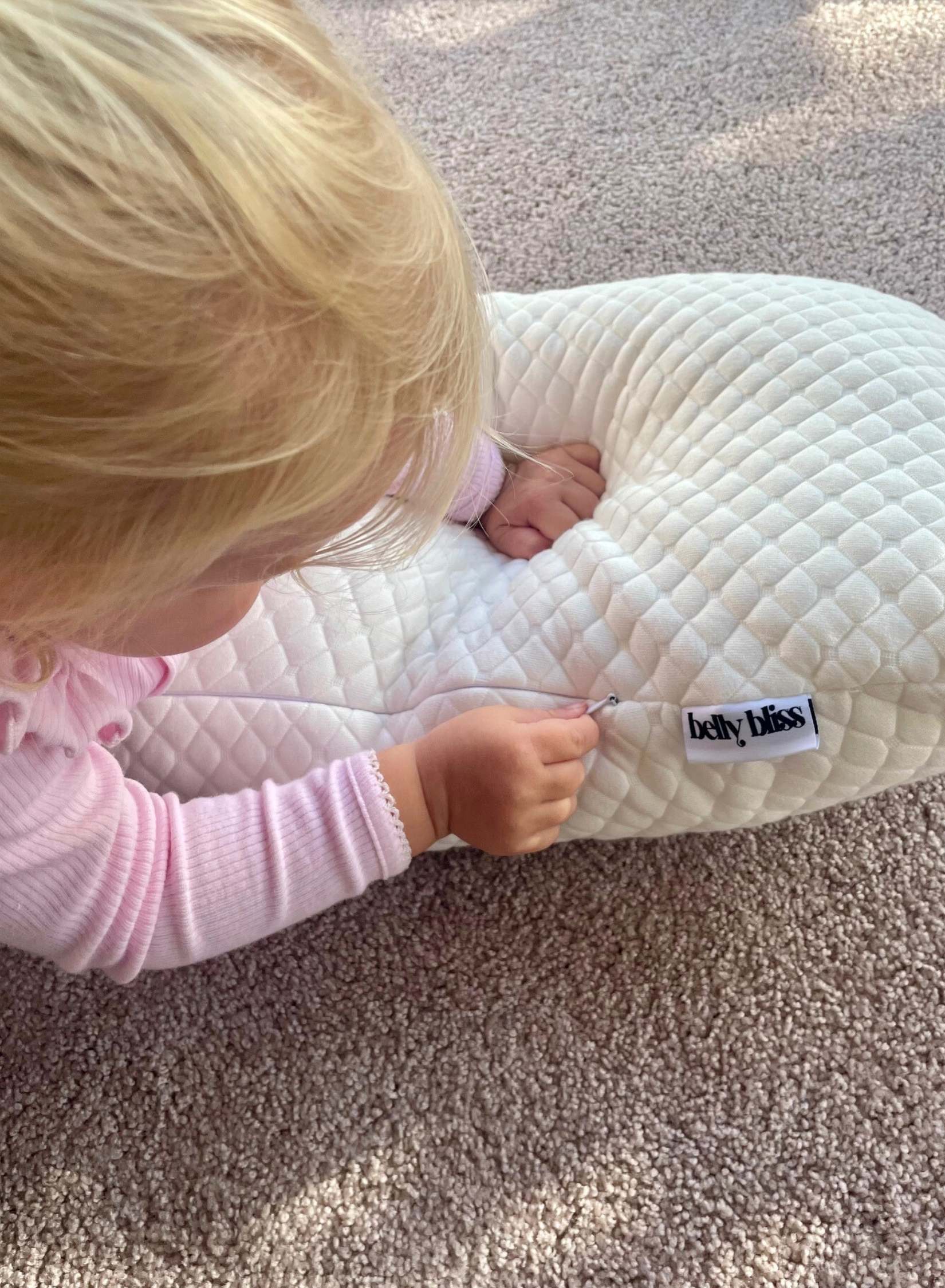 Child interacting with a white pregnancy pillow on a carpeted floor