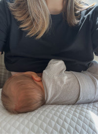 Baby lying on a bed next to an adult wearing a black shirt