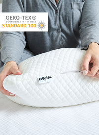 Person holding a white belly pillow with 'belly bliss' branding, OEKO-TEX Standard 100 logo visible.