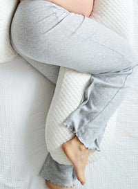 Person wearing light gray sweatpants using a pregnancy pillow on bed