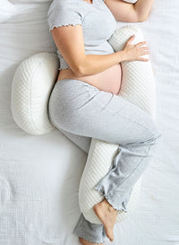 Pregnant person using a pregnancy pillow on a bed