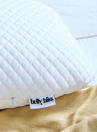 White quilted pillow with 'belly bliss' label on a beige fabric background