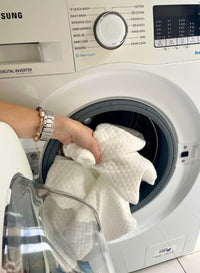 Person taking a white pillow out of a washing machine with a Samsung dryer in the background.