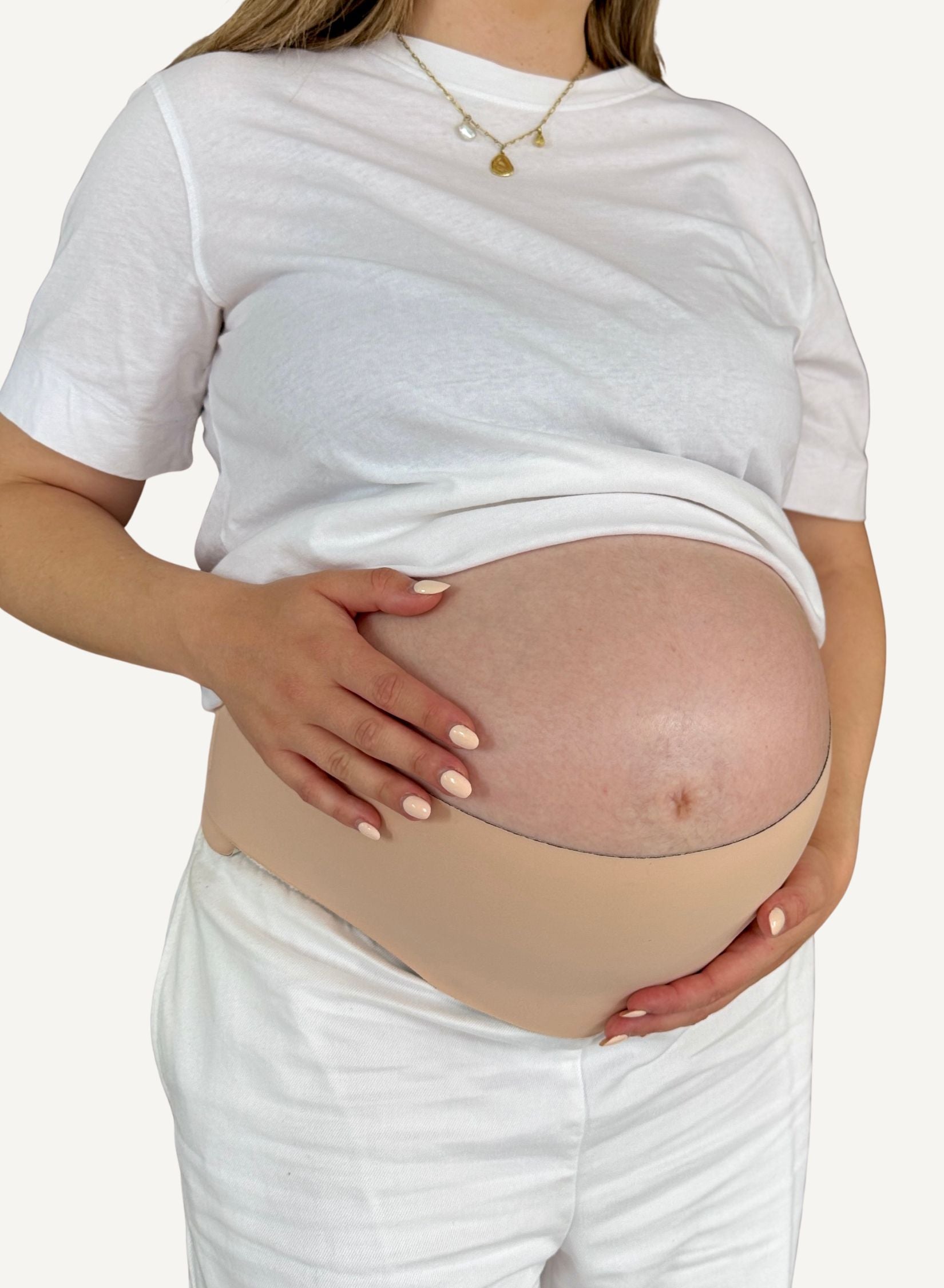Pregnant person wearing a beige maternity support belt with a white t-shirt and pants.