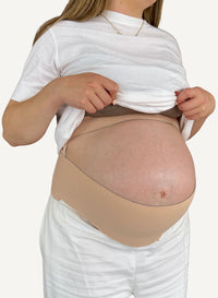Person wearing a beige belly band over a white shirt and pants on a plain background