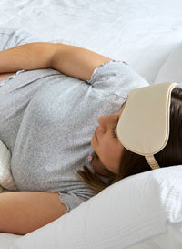 Person lying on a bed wearing a beige eye mask on their head.
