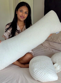 Woman holding a large white pregnancy pillow on a bed