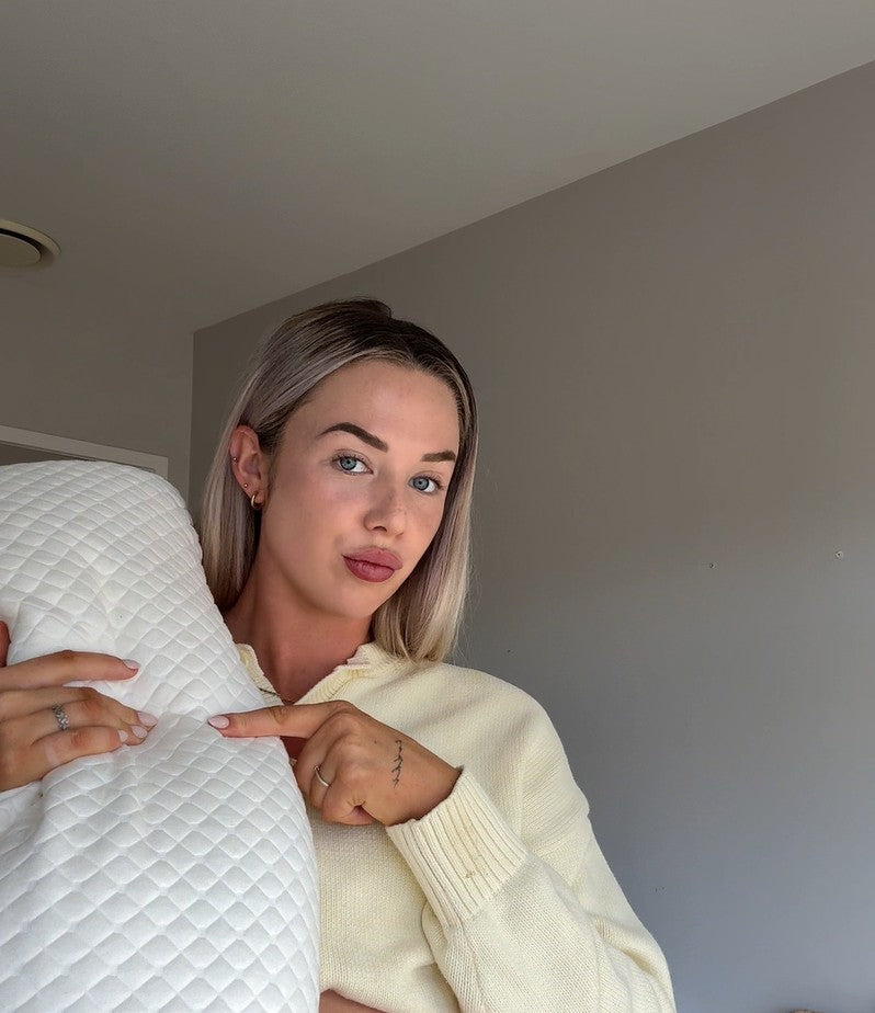 Woman pointing at a white pillow against a plain wall