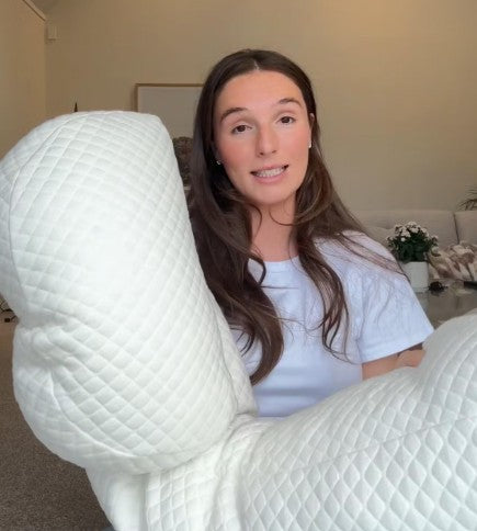 Person holding a large white pillow in a home setting