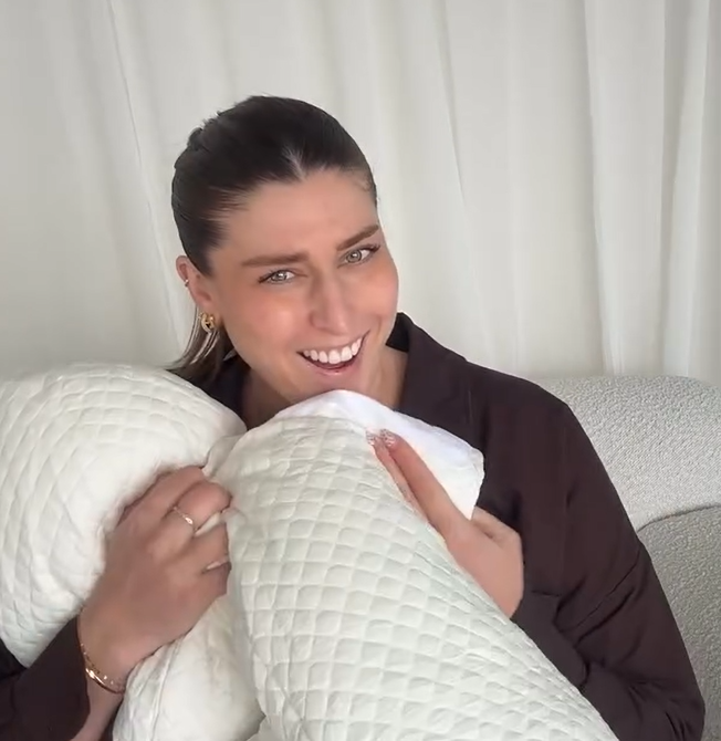 Woman holding two white pillows against a neutral background