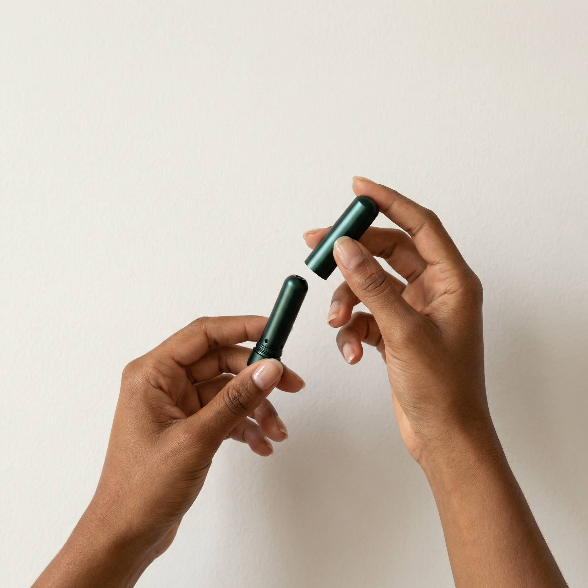 Two hands holding a green cylindrical object against a light background