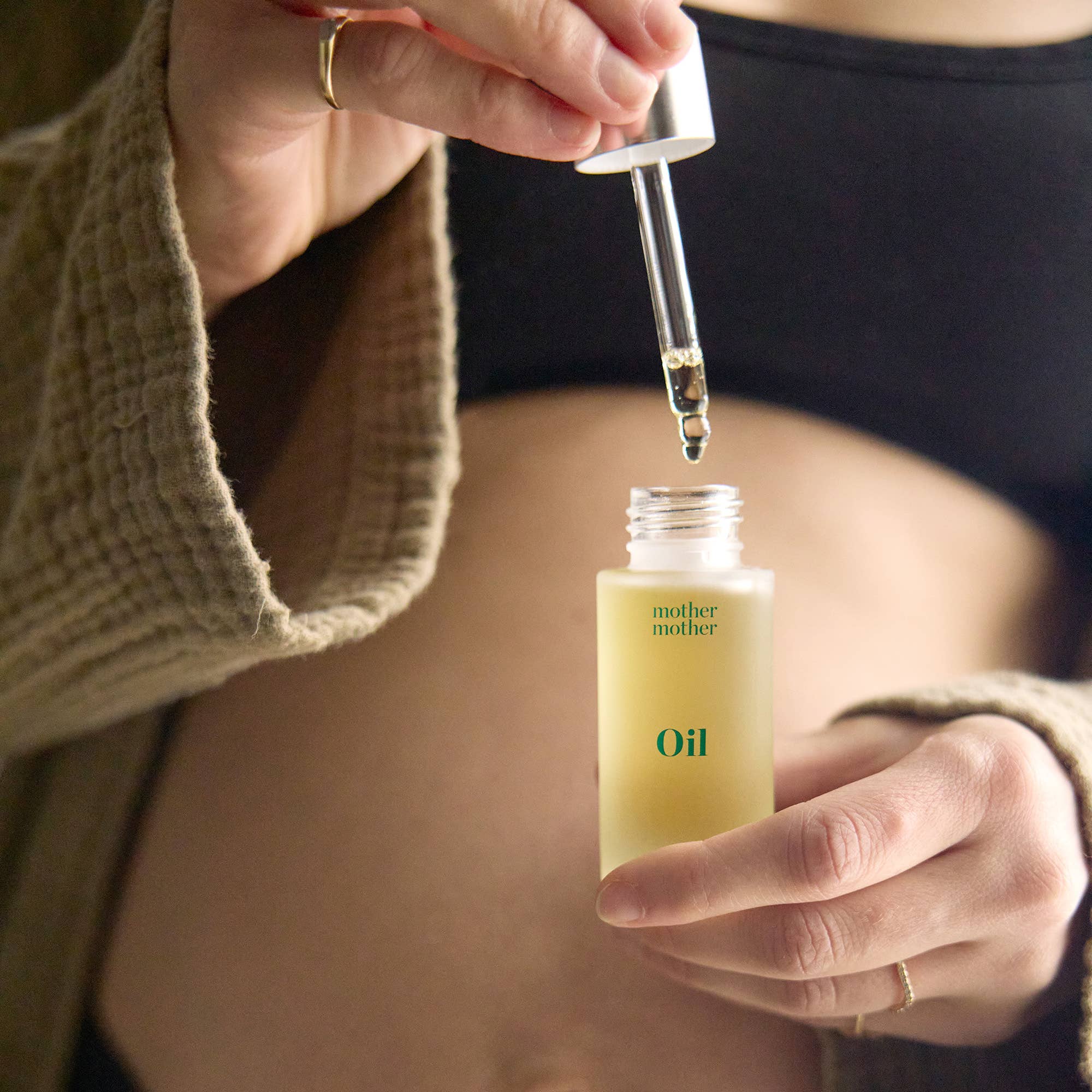 Person holding a bottle of 'mother mother' oil with a dropper.