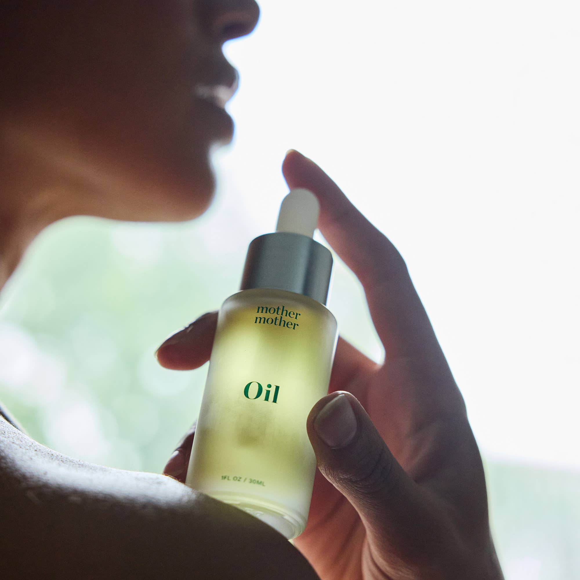 Hand holding a bottle of 'mother' oil with a blurred background