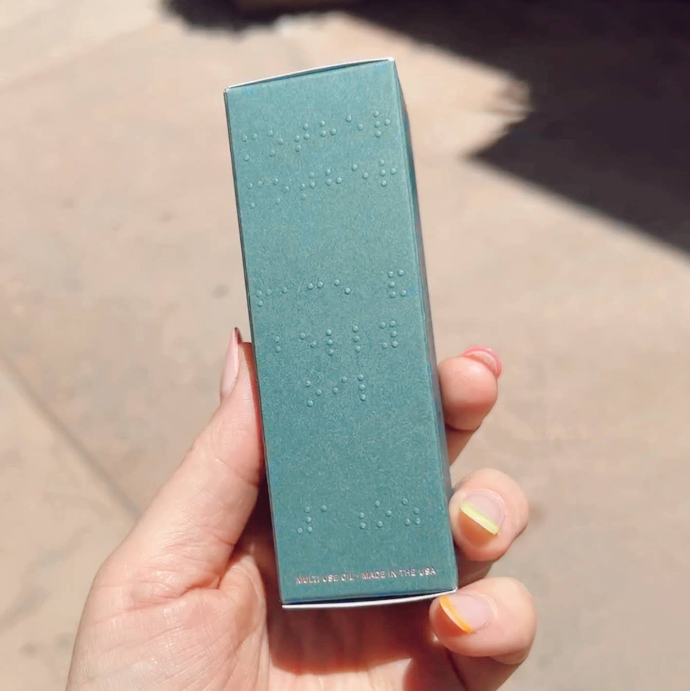 Hand holding a teal box with text, against a neutral background