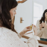 Woman holding a bottle of oil in front of a mirror
