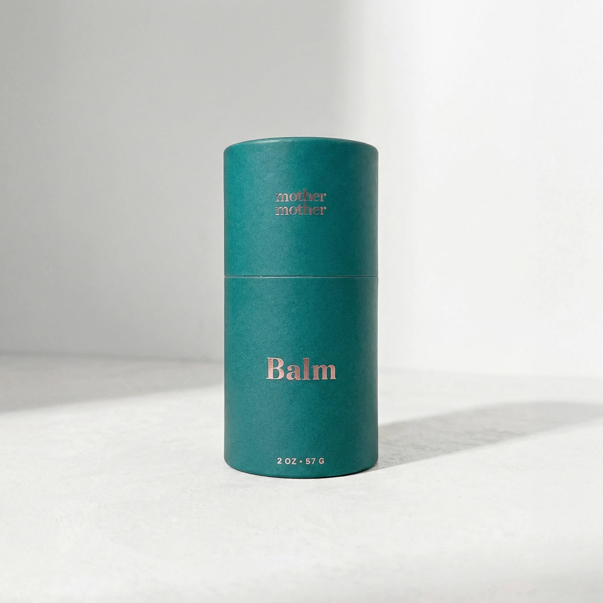 Teal cylindrical balm container with 'mother' branding on a light gray background