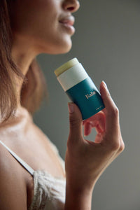 Woman holding a blue skincare stick with a neutral background