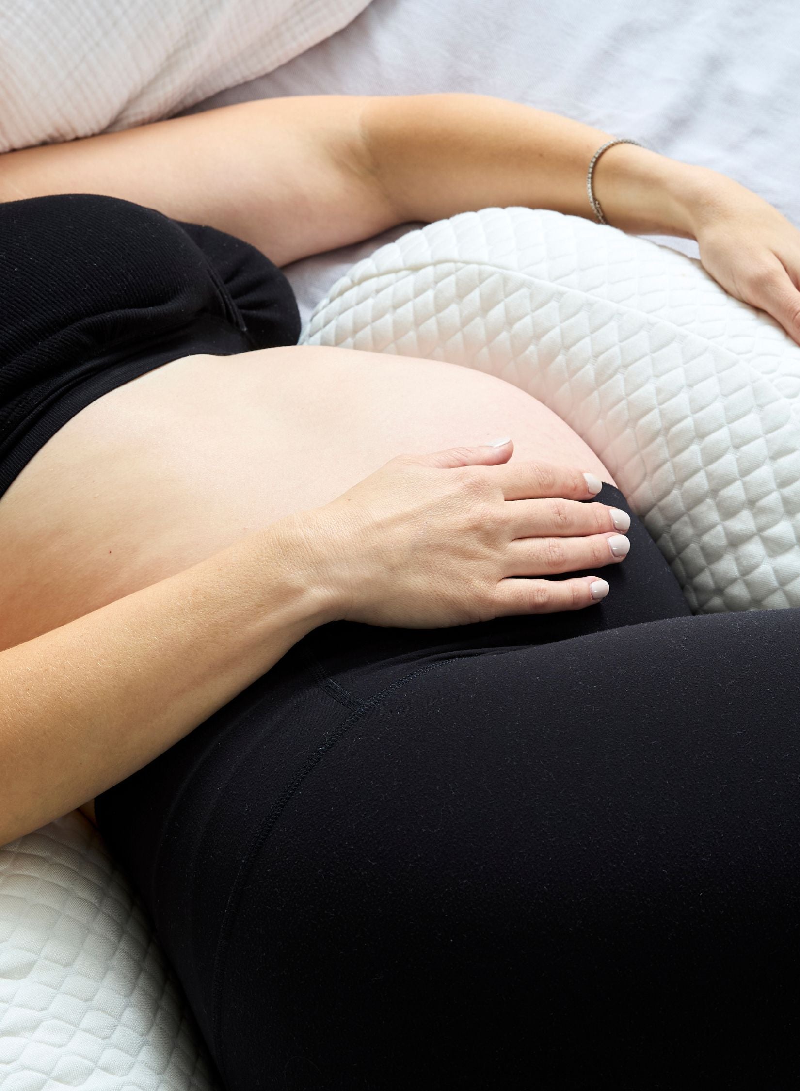 Person lying on a white pregnancy pillow with their hand on their stomach