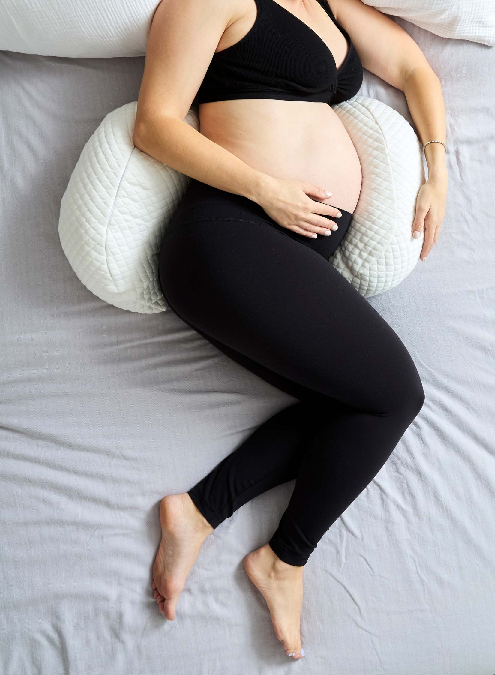 Pregnant person using a wedge prengancy pillow on a bed